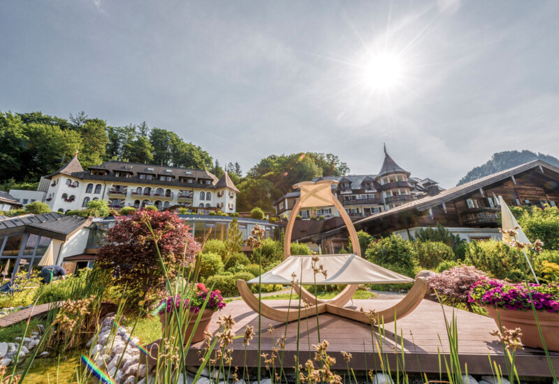 Luxurious hotel surrounded by lush gardens under a bright sun, offering a scenic backdrop.