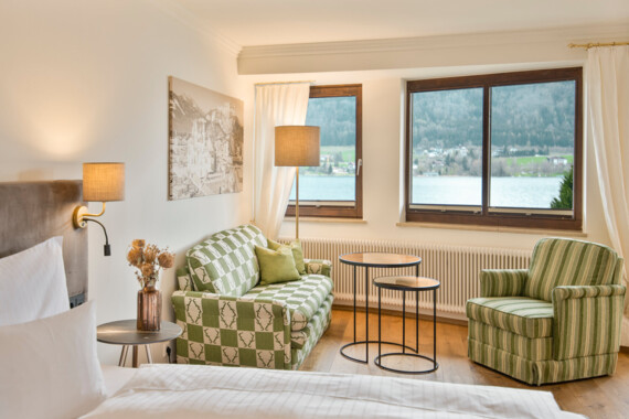 Bright room with patterned furniture, large windows showcasing a lake and mountain view, and a cozy ambiance.