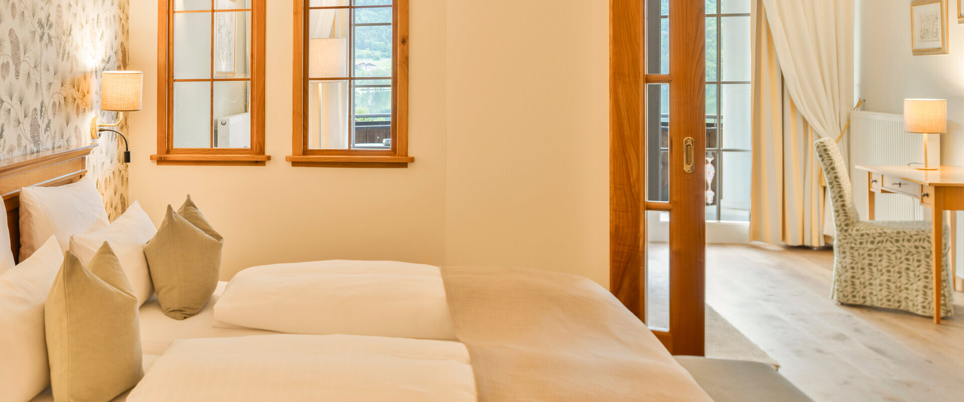 Elegant hotel room with cozy bedding, warm lighting, and wooden accents, featuring a view through arched windows.