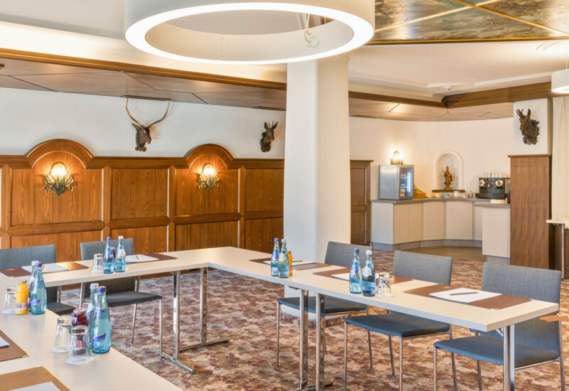 A well-lit conference room with a U-shaped table setup, chairs, and bottled water. Deer mounts and wood paneling decorate the walls.