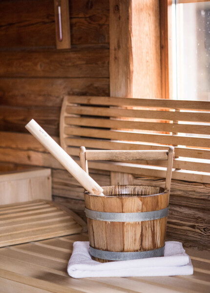 A wooden sauna bucket with a ladle on a bench inside a rustic sauna room.