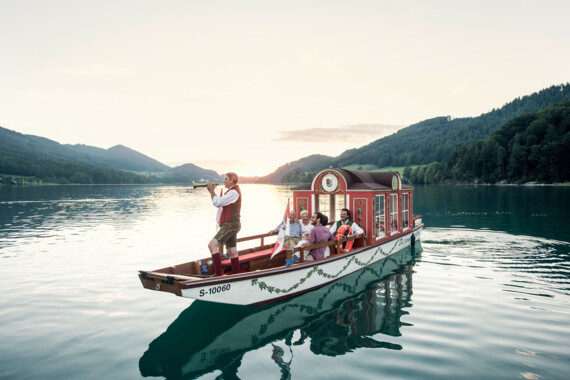 A boat with people in traditional attire sails on lake Fuschl.
