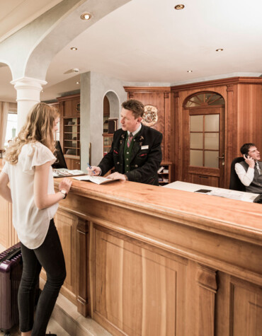 Woman checking in at hotel reception desk, with staff assisting and luggage nearby.