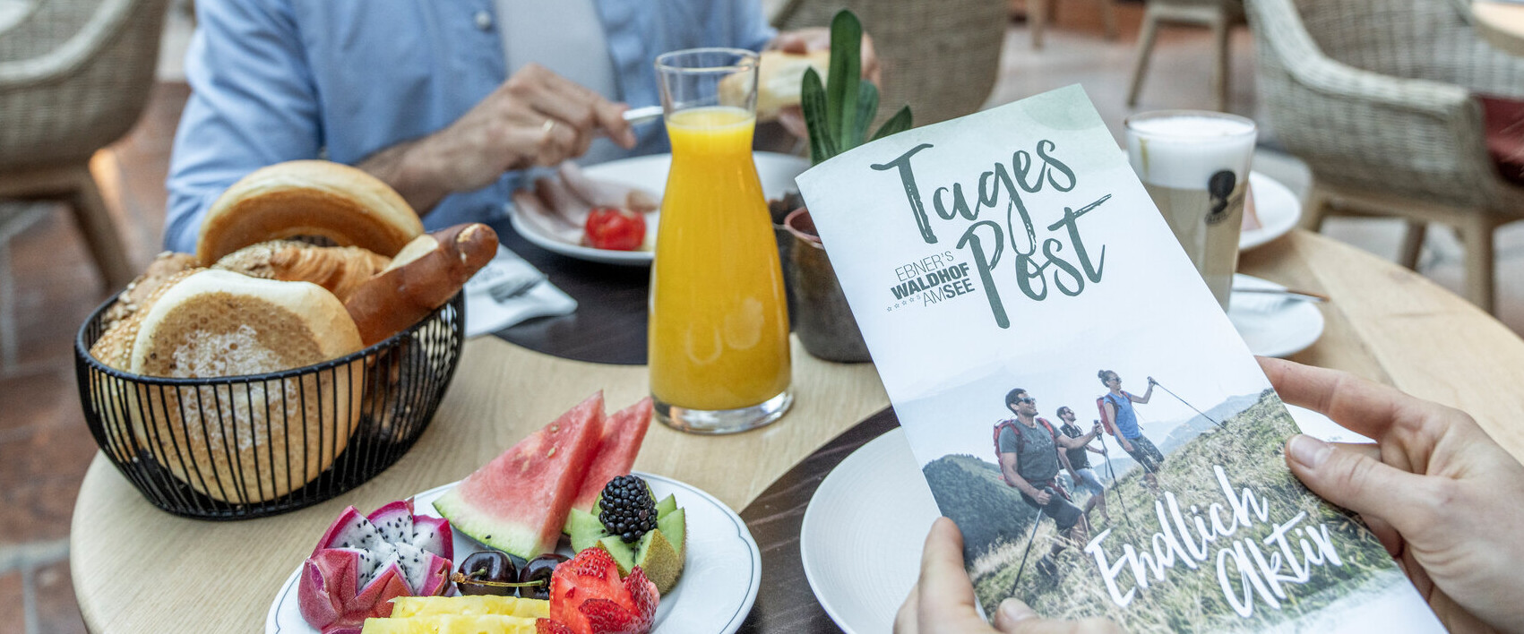 People enjoying breakfast, with a focus on a brochure titled "Tages Post" on the table.