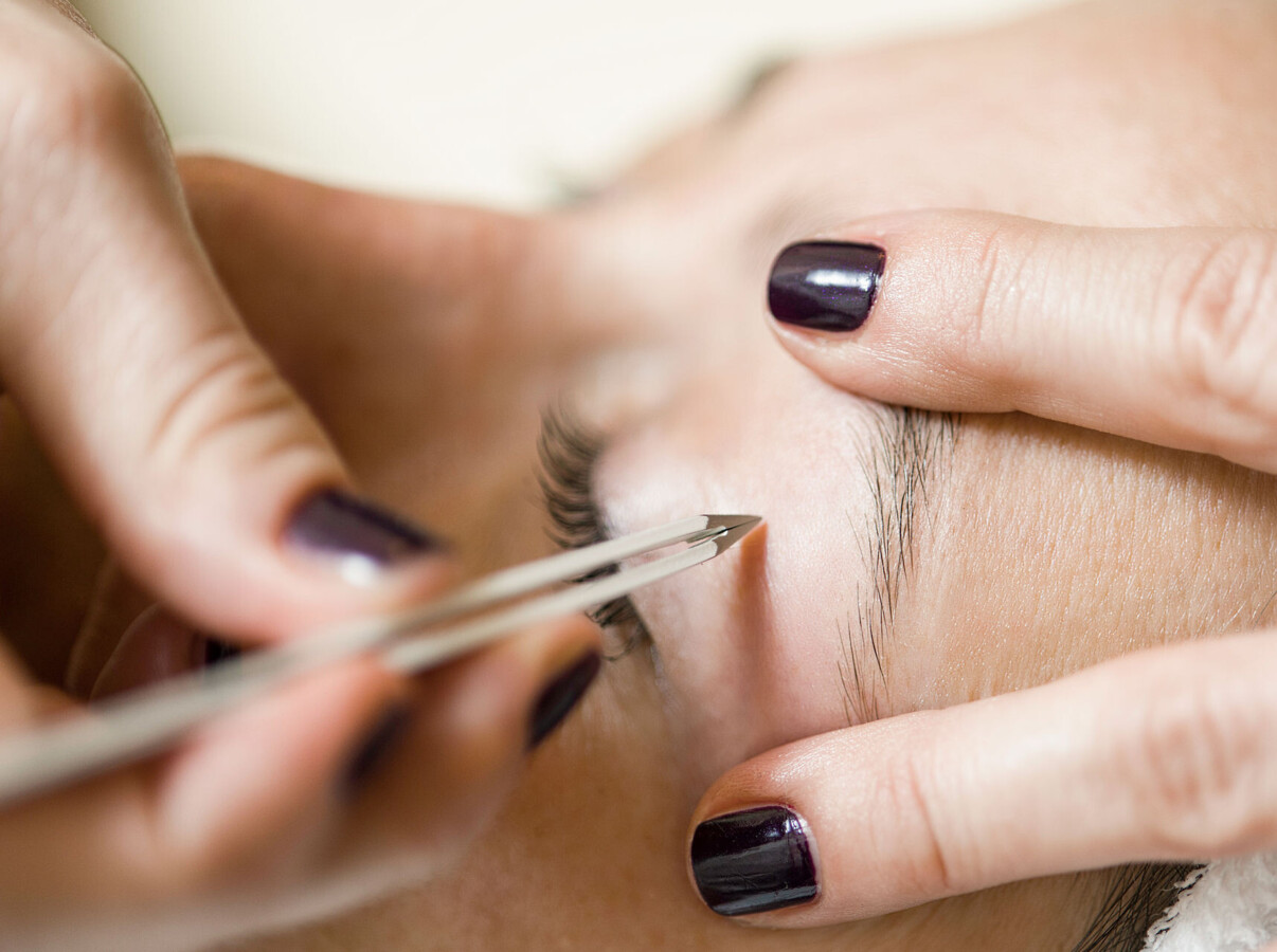 Eyebrow being carefully shaped with tweezers during a beauty treatment.