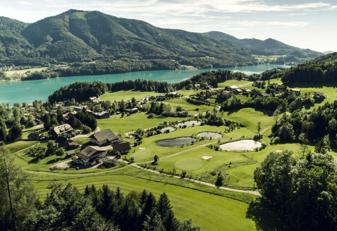 Aerial view of a golf course surrounded by mountains and Fuschlsee.