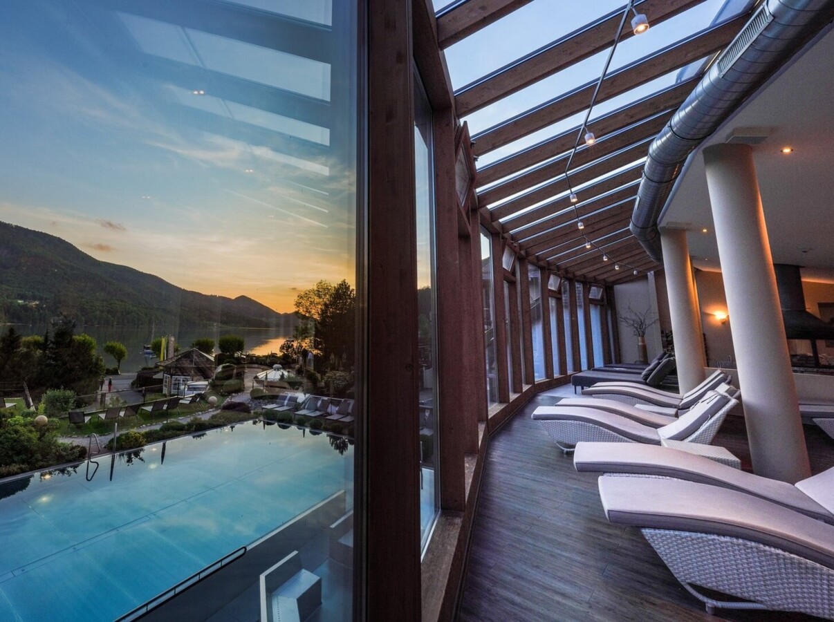 Scenic view from Waldhof Fuschlsee Resort's indoor pool area, overlooking Lake Fuschl and mountains at sunset.