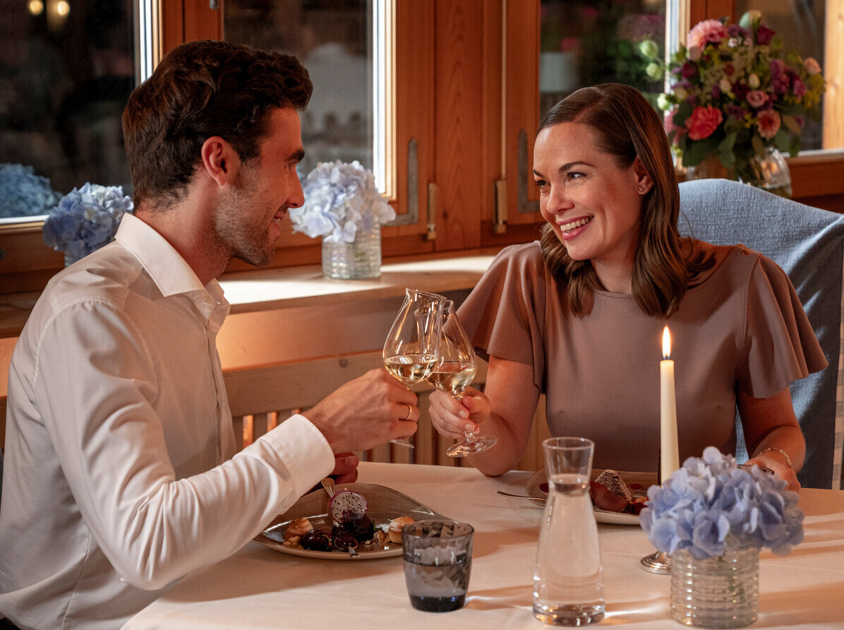 A couple enjoying a romantic dinner in a cozy, elegantly decorated restaurant with flowers and candlelight.