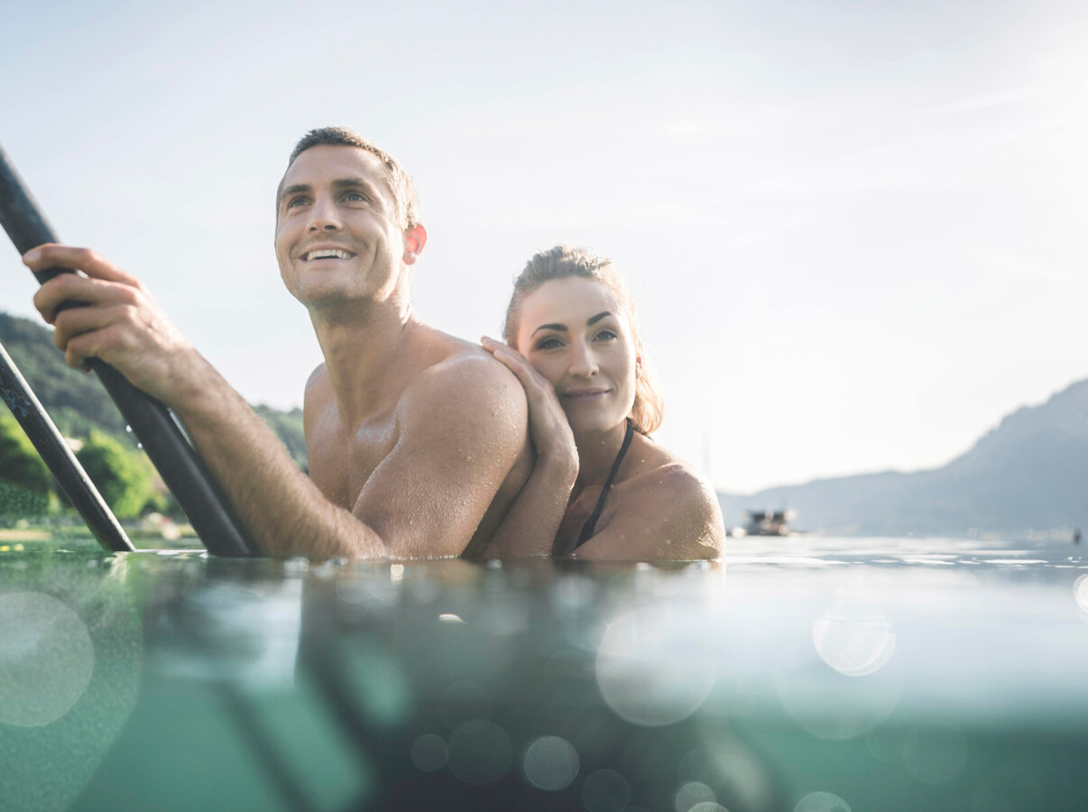 Pärchen an der Leiter eines Badestegs beim Baden im Attersee, Salzkammergut.