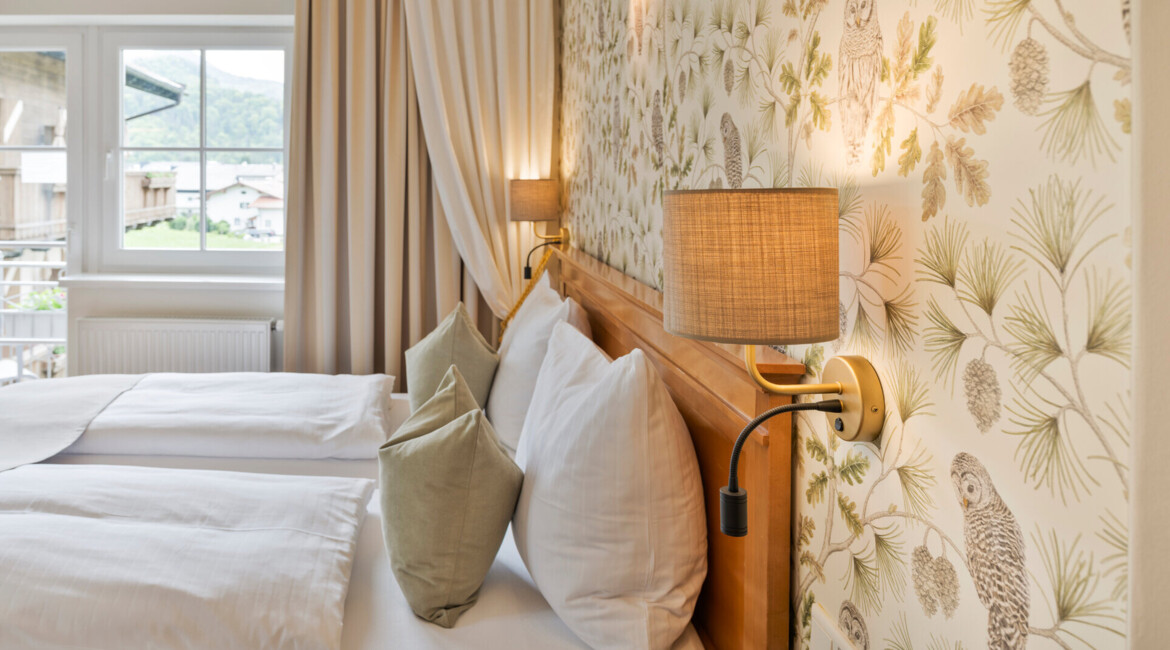 Elegant hotel room with twin beds, nature-themed wallpaper, and a view of scenic mountains through the window.