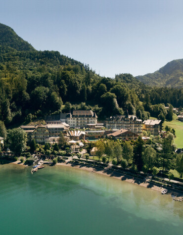 Luftaufnahme Waldhof Fuschlsee Resort, umgeben von Wald und Bergen, mit Booten auf dem Fuschlsee.