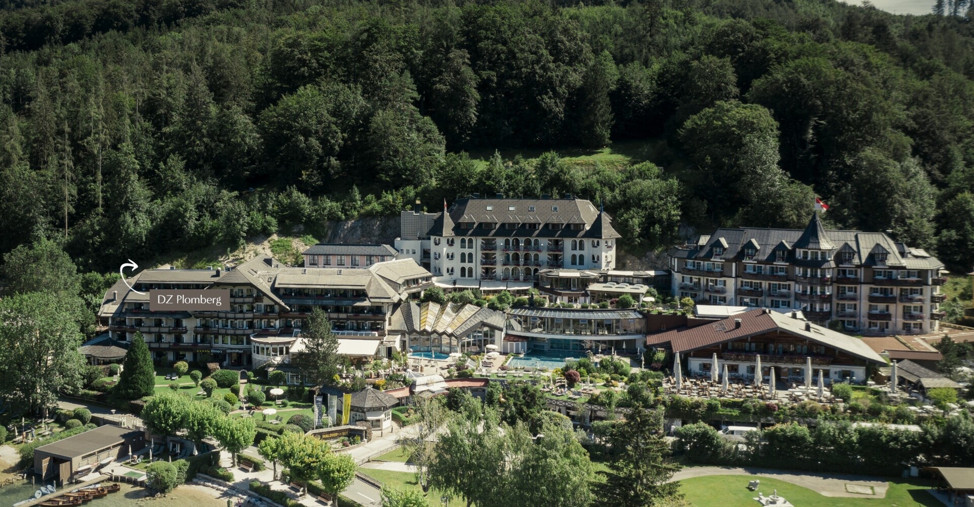 Aerial view of a scenic hotel surrounded by lush greenery, located near a lake.